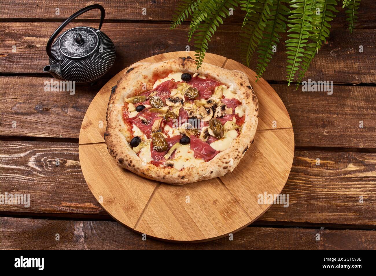 Köstliche Pizza Capriciosa auf einem Holzständer Stockfoto
