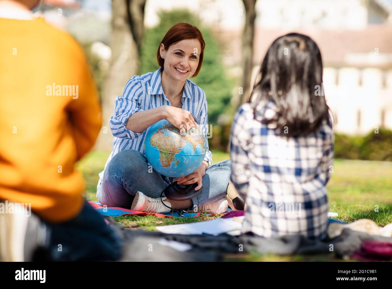 Lehrer mit kleinen Kindern sitzen im Freien im Stadtpark, Lerngruppe Bildungskonzept. Stockfoto