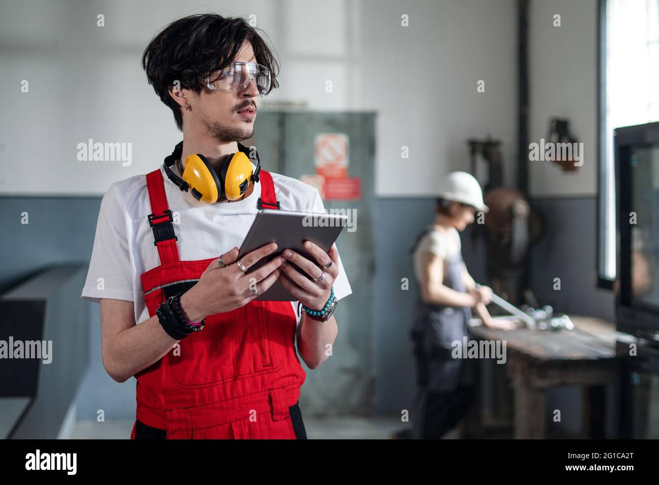 Porträt eines jungen Arbeiters, der in der Fabrik steht und die Kamera anschaut. Stockfoto
