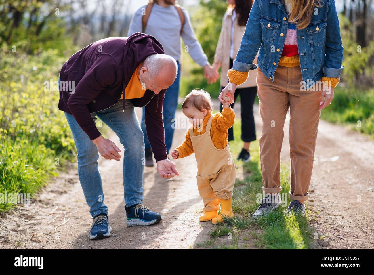 Kleines Kleinkind mit unverkennbaren Eltern und Großeltern auf einem Spaziergang im Freien in der Natur. Stockfoto