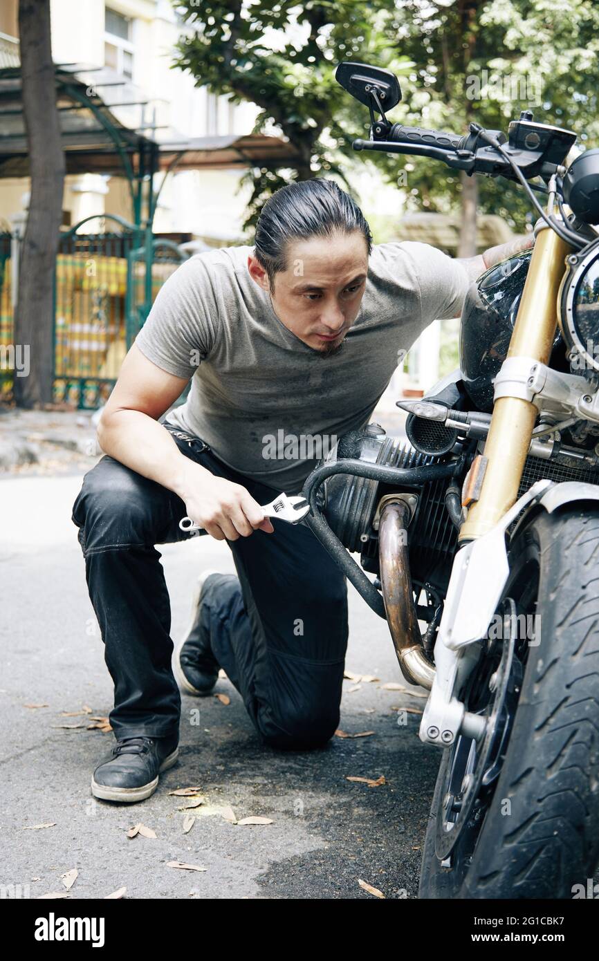 Serious nachdenklichen Mechaniker mit Schraubenschlüssel in der Hand Befestigung Motor Motorrad im Freien Stockfoto