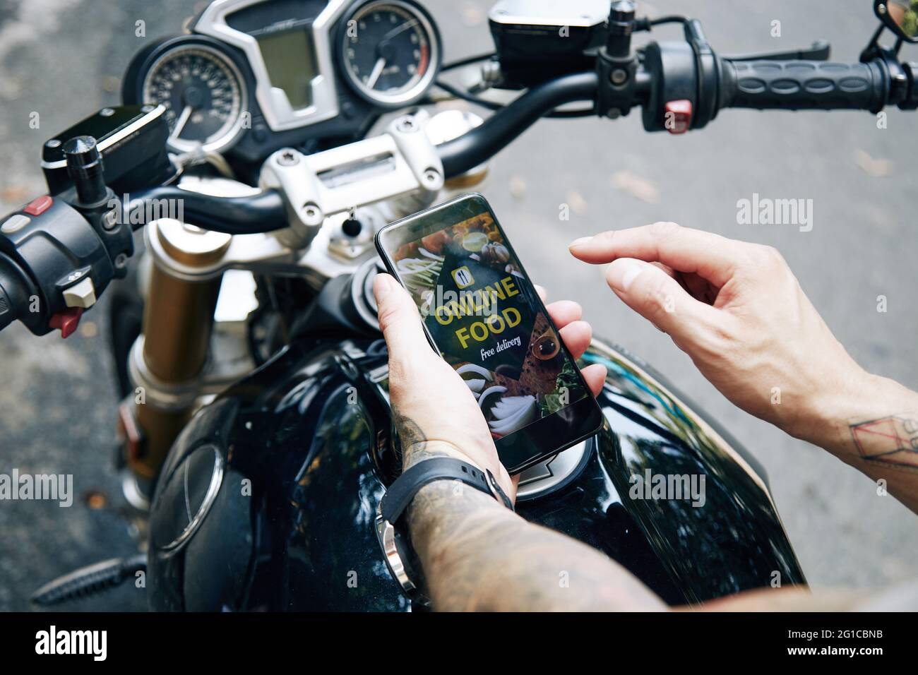 Hände eines Mannes, der auf dem Motorrad sitzt und mit einer mobilen Anwendung Lebensmittel aus dem lokalen Café bestellt Stockfoto