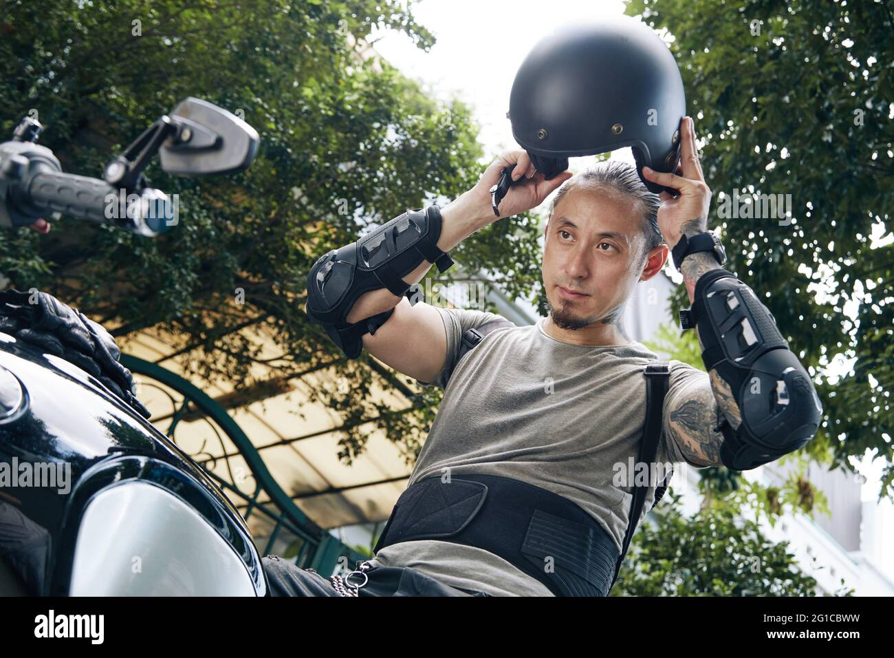 Schöner ernster Mann, der vor dem Motorradfahren Ausrüstung und Helm aufsetzt Stockfoto