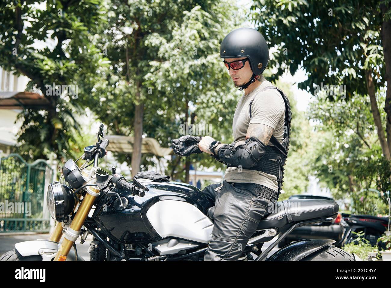 Motorradfahrer in Fahrausrüstung, Helm und Brille, die Lederhandschuhe anziehen, wenn sie auf dem Fahrrad sitzen Stockfoto