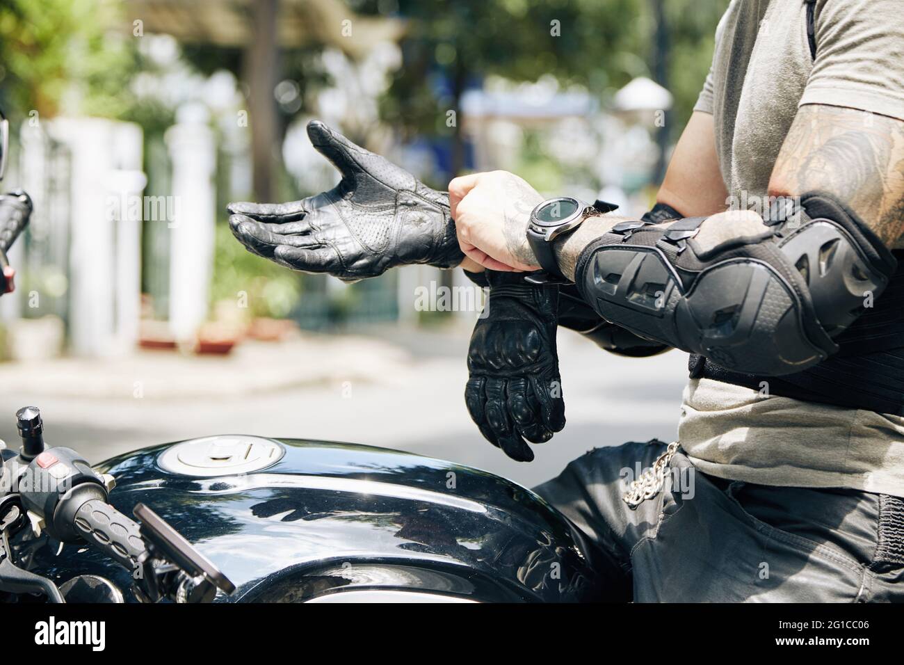 Hände von Motorradfahrern, die auf dem Fahrrad sitzen und Fahrausrüstung wie Unterarmschützer und Lederhandschuhe anziehen Stockfoto