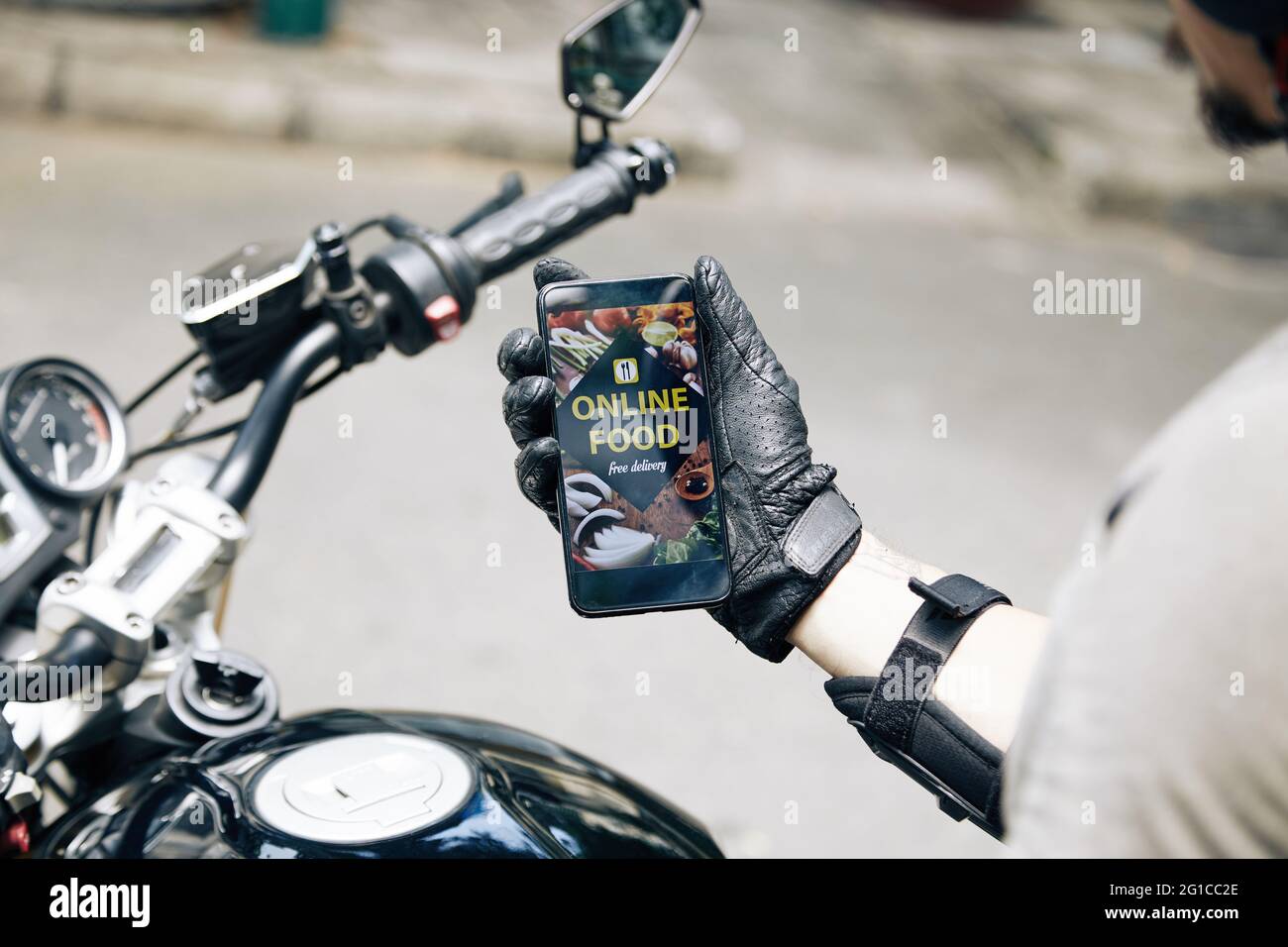 Hände eines Kuriers auf dem Motorrad, der die Anwendung zur Lebensmittelzustellung auf seinem Smartphone überprüft Stockfoto