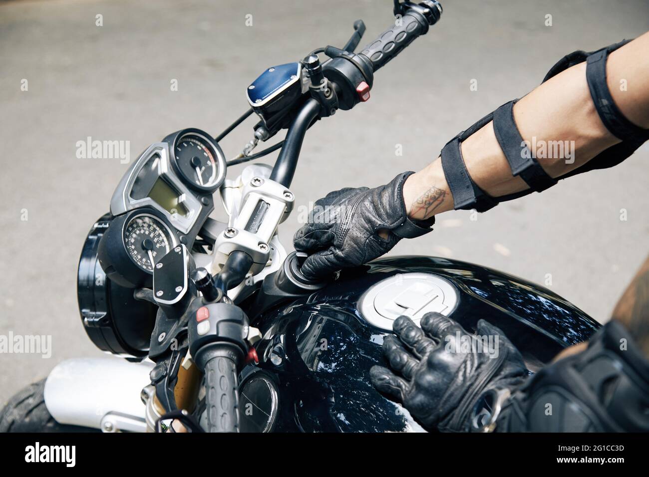 Hände eines Mannes in Lederhandschuhen, die den Benzintank seines Motorrads öffnen Stockfoto