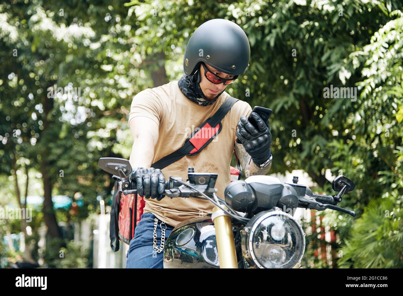 Deliveryman im Helm sitzt auf dem Motorrad und Überprüfung der Adresse des Kunden über die Anwendung auf dem Smartphone Stockfoto