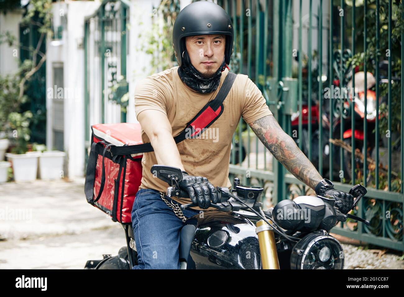 Porträt eines ernsthaften Deliveryman im Helm, der auf dem Motorrad fährt, wenn er Bestellungen an Kunden liefert Stockfoto