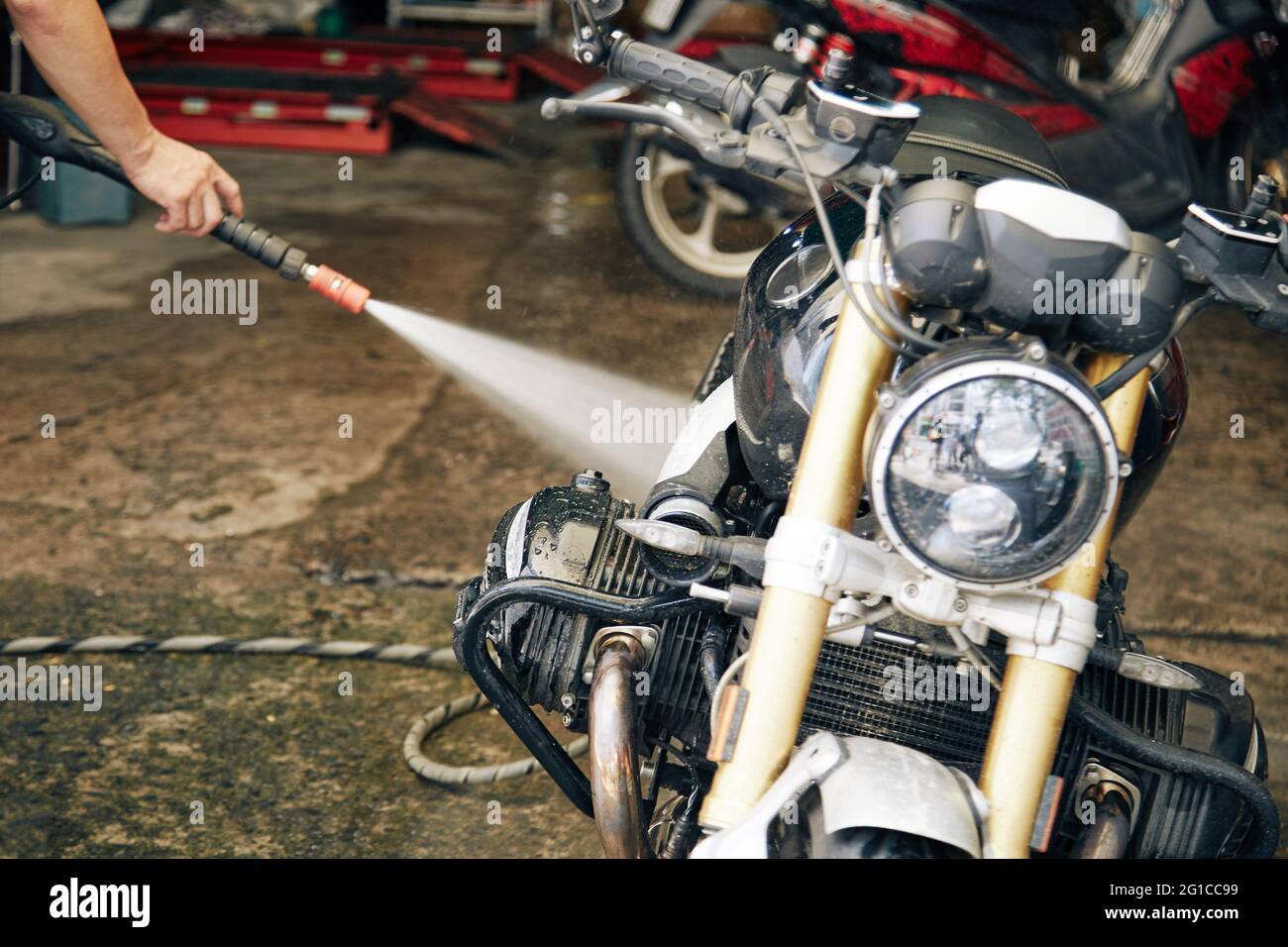 Mann, der sein Motorrad in der Garage mit Wasser spülte, nachdem er auf einer schlammigen Straße gefahren war Stockfoto