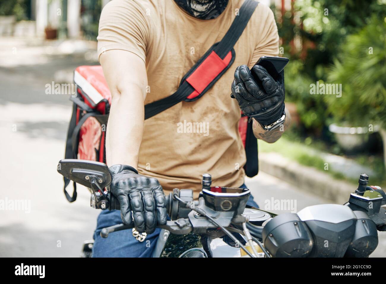 Zugeschnittenes Bild des Lieferers, der auf dem Motorrad sitzt und die mobile Anwendung auf neue Bestellung überprüft Stockfoto