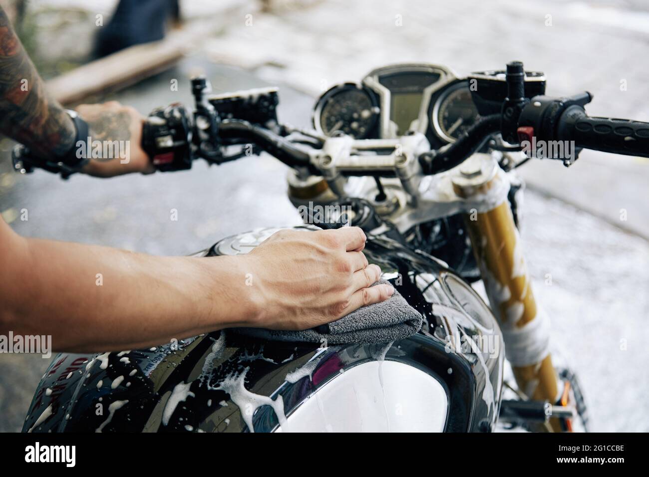 Hände eines Mannes, der mit einem weichen Tuch Reinigungsschaum von seinem Motorrad abwischt Stockfoto