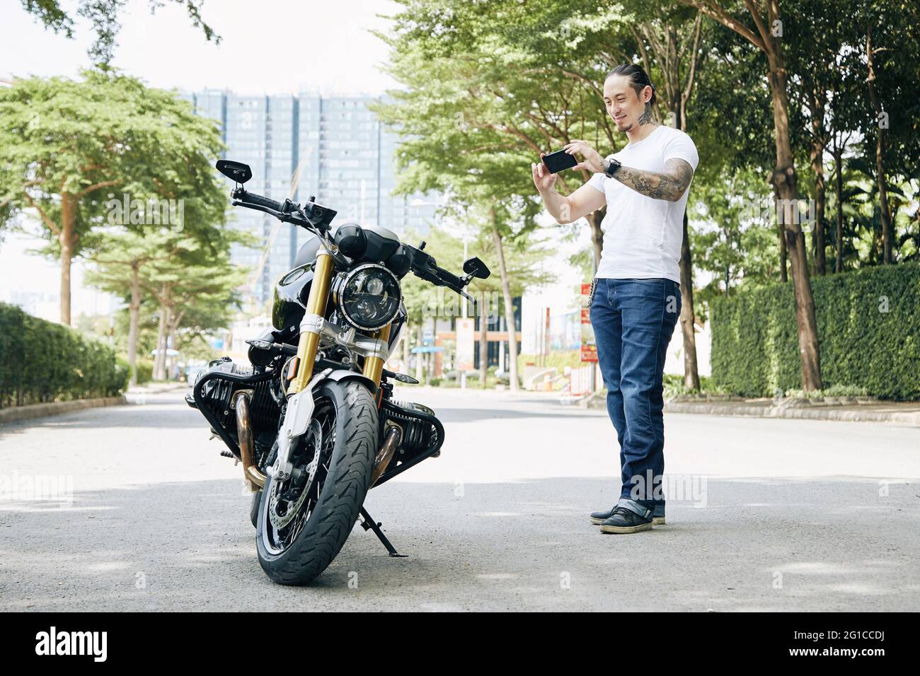Ein glücklicher, fund Mann fotografiert Motorrad auf dem Smartphone, um es in den sozialen Medien zu posten Stockfoto