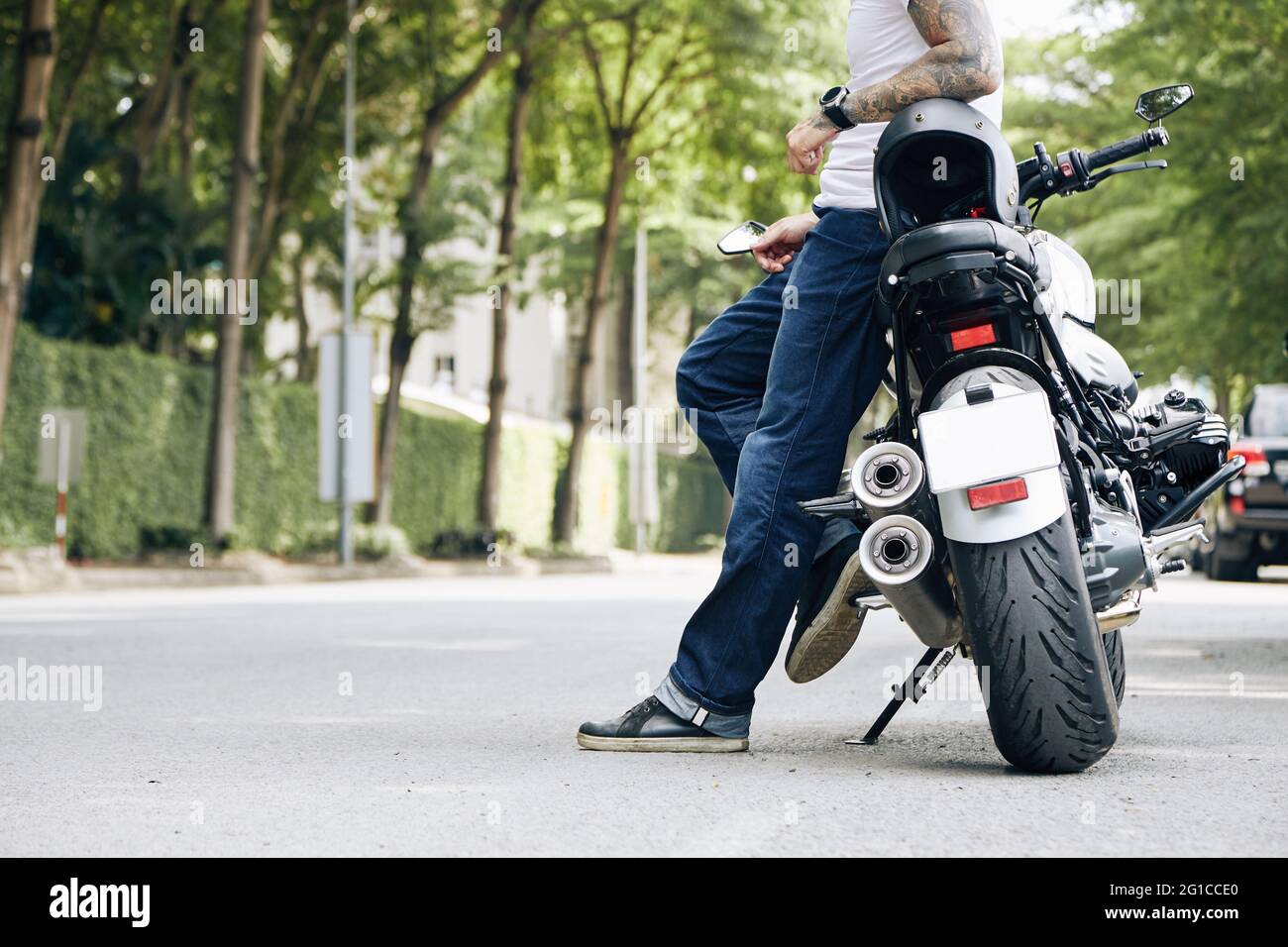 Fit Mann in Jeans und weißem T-Shirt auf der Straße stehen und auf dem Motorrad gelehnt Stockfoto