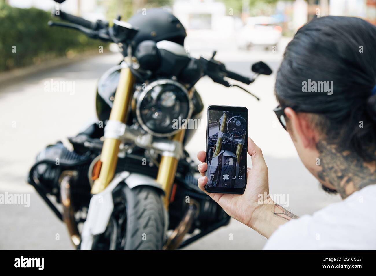 Mann, der coole Fotos von seinem Motorrad auf dem Smartphone gemacht hat, um es mit Freunden zu teilen oder in den sozialen Medien zu posten Stockfoto