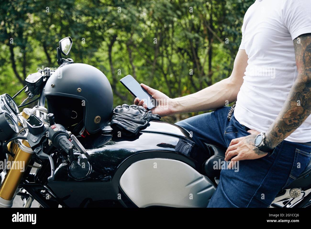 Mann, der auf dem Motorrad sitzt und die Navigatoranwendung auf seinem Smartphone einsetzt Stockfoto