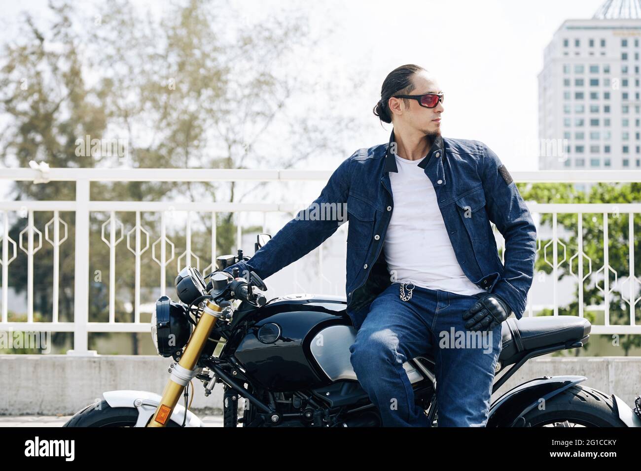 Portrait eines coolen stylischen Mannes in Sonnenbrille, der auf dem Motorrad sitzt und wegschaut Stockfoto