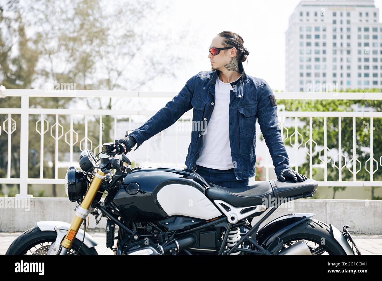 Ernsthafter Mann in Sonnenbrille, der auf dem Motorrad steht und wegschaut Stockfoto