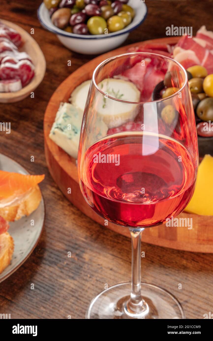 Ein Glas Rosenwein aus nächster Nähe mit einem Käse- und Aufschnitt-Brett im Hintergrund, mit Oliven und Lachs-Sandwiches. Tapas oder Antipasti in einer Bar Stockfoto
