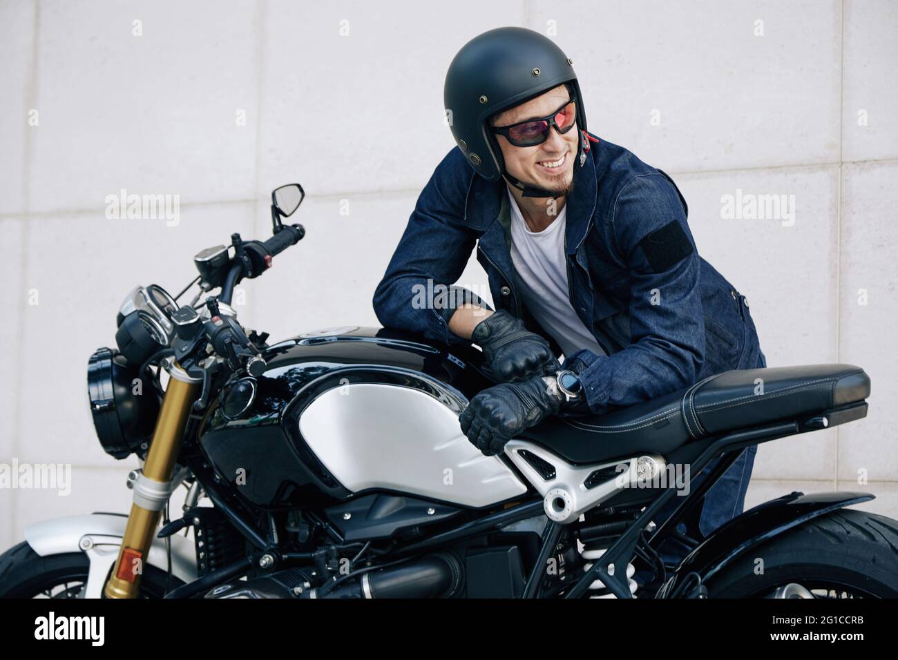 Porträt eines glücklichen lächelnden Mannes im Helm, der sich auf dem Motorrad lehnt und wegschaut Stockfoto
