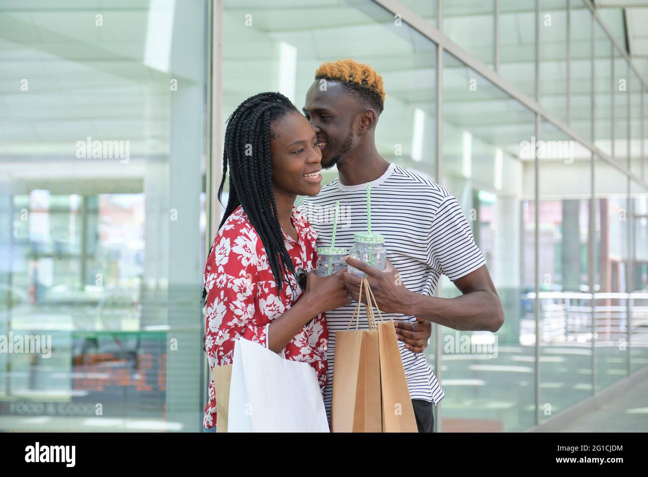 Junges afrikanisches Paar trinkt erfrischende Getränke und geht einkaufen, umarmt und flüstert. Stadtleben Konzept. Stockfoto