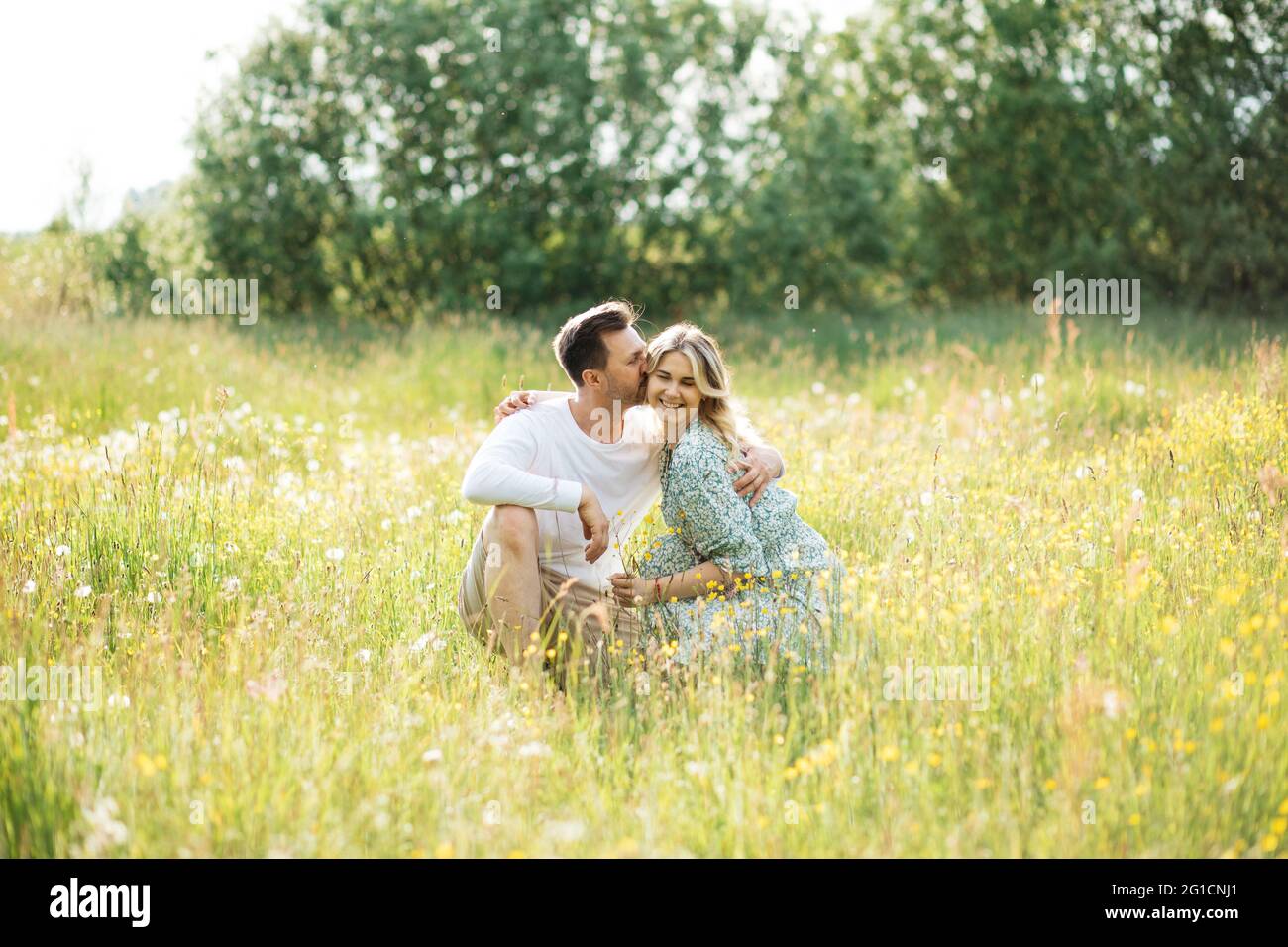 Der Mann umarmt seine Geliebte auf der Wiese zwischen Wildblumen, Konzept der Dating, verliebt sich Stockfoto