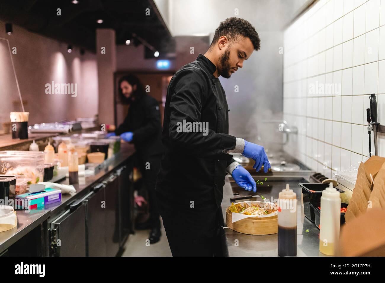 Der männliche Kellner streute in der Schüssel Frühlingszwiebeln auf Knödel über die Küchentheke im Restaurant Stockfoto