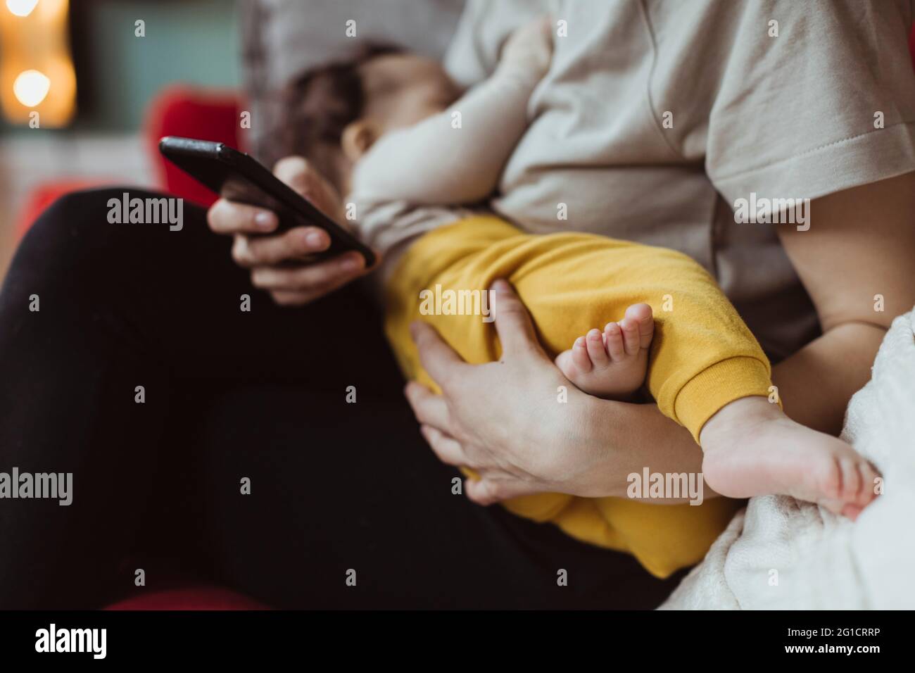 Mittelteil der Mutter mit Baby Junge mit Smartphone im Wohnzimmer Stockfoto