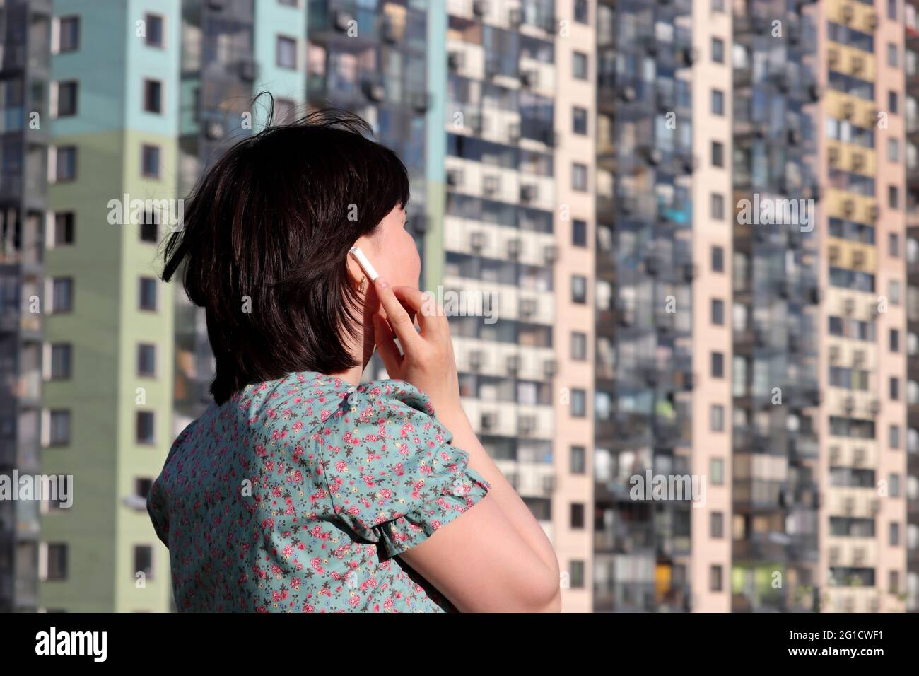 Frau berührt den kabellosen Kopfhörer im Ohr, der im Hintergrund eines Wohngebäudes steht. Headset, Musik hören und Sprachanruf-Konzept Stockfoto