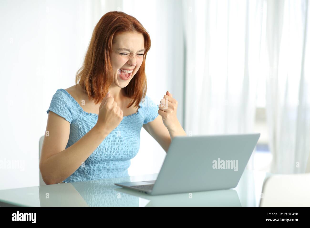 Eine aufgeregte Frau, die ihren Laptop verwendet, feiert den Erfolg in einem Hotelzimmer Stockfoto