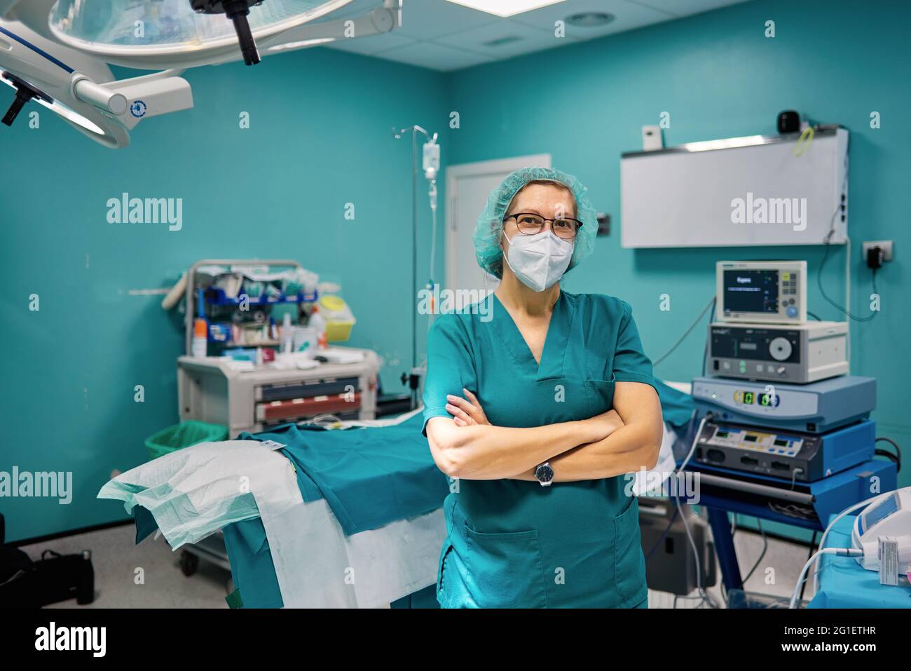 Selbstbewusste Ärztin in medizinischer Uniform, die im Krankenhaus mit gefalteten Armen auf die Kamera schaut Stockfoto