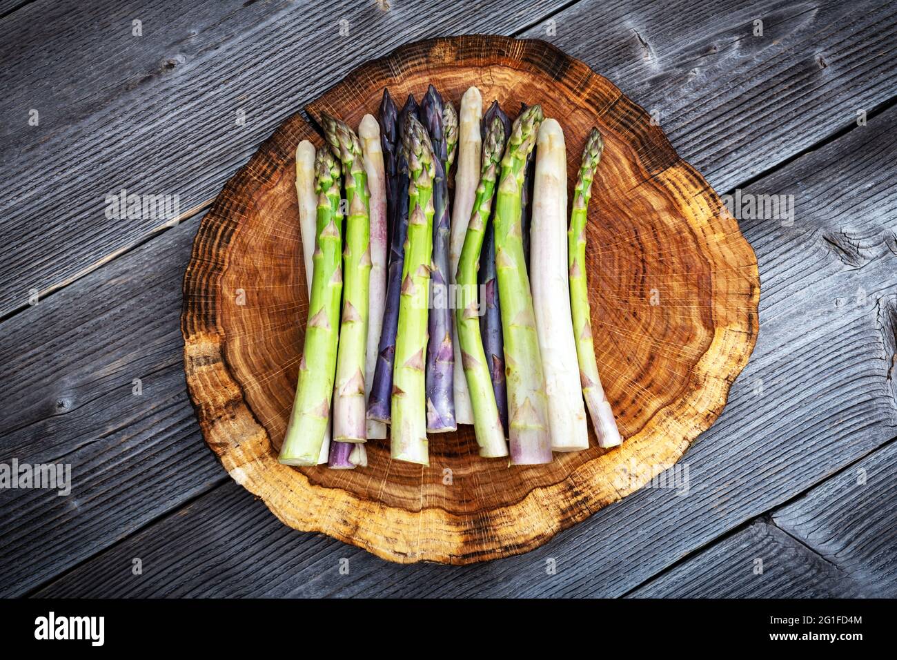 Grüner, violetter und weißer Spargel sprießt auf Holzbrett aus der Nähe. Draufsicht flach liegend. Food-Fotografie Stockfoto