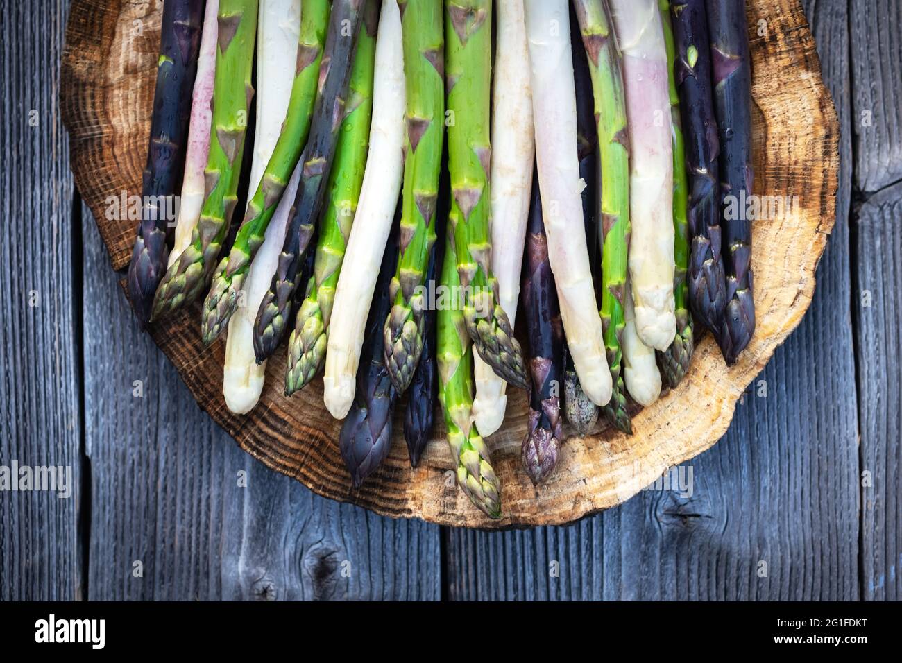 Grüner, violetter und weißer Spargel sprießt auf Holzbrett aus der Nähe. Draufsicht flach liegend. Food-Fotografie Stockfoto