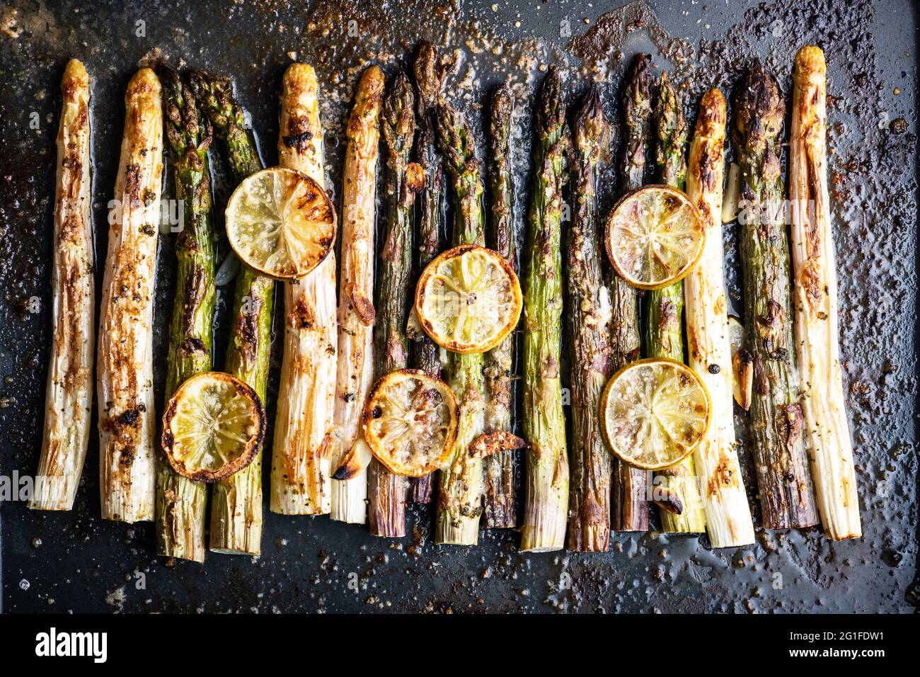 Gebackene weiße, violette und grüne Spargel sprießen Gemüse mit Zitrone, Knoblauch und Käse auf einem dunklen Hintergrund. Food-Fotografie Stockfoto