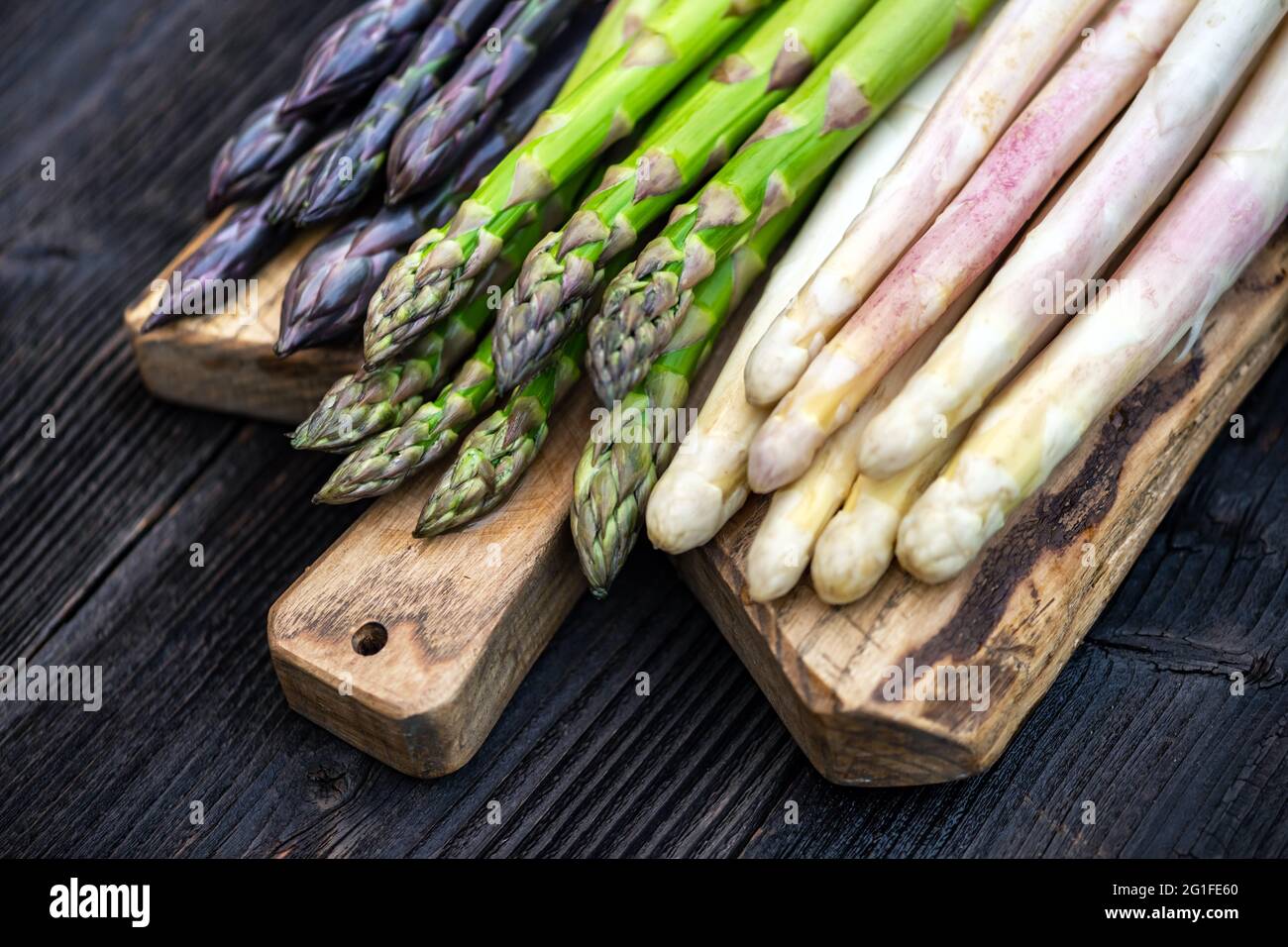 Grüner, violetter und weißer Spargel sprießt auf Holzbrett aus der Nähe. Draufsicht flach liegend. Food-Fotografie Stockfoto
