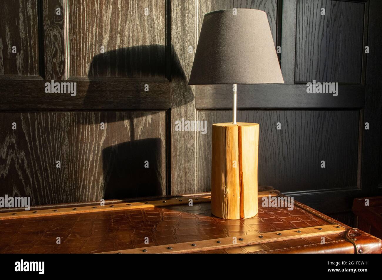 Einzelne Lampe auf der Tischplatte vor einer dunkel getäfelten Wand in natürlichem Licht, die ihren Schatten auf die Wand mit Kopierraum wirft Stockfoto