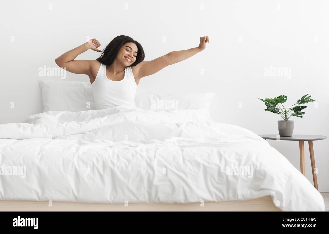 Guten Morgen, neuer Tag. Aufgeregte afroamerikanische Dame, die auf dem Bett sitzt, nach dem Schlaf die Arme streckt und Platz frei macht Stockfoto