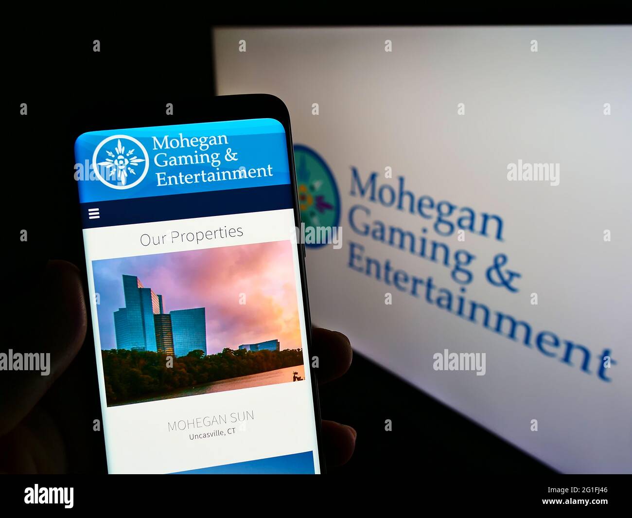 Person mit Mobiltelefon und Webseite des US-Unternehmens Mohegan Gaming and Entertainment (MGE) auf dem Bildschirm mit Logo. Konzentrieren Sie sich auf die Mitte des Telefondisplays. Stockfoto