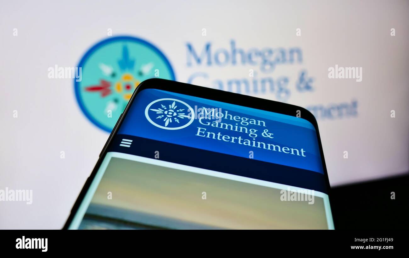 Person mit Smartphone und Website des US-Unternehmens Mohegan Gaming and Entertainment (MGE) auf dem Bildschirm mit Logo. Konzentrieren Sie sich auf die obere linke Seite des Telefondisplays. Stockfoto