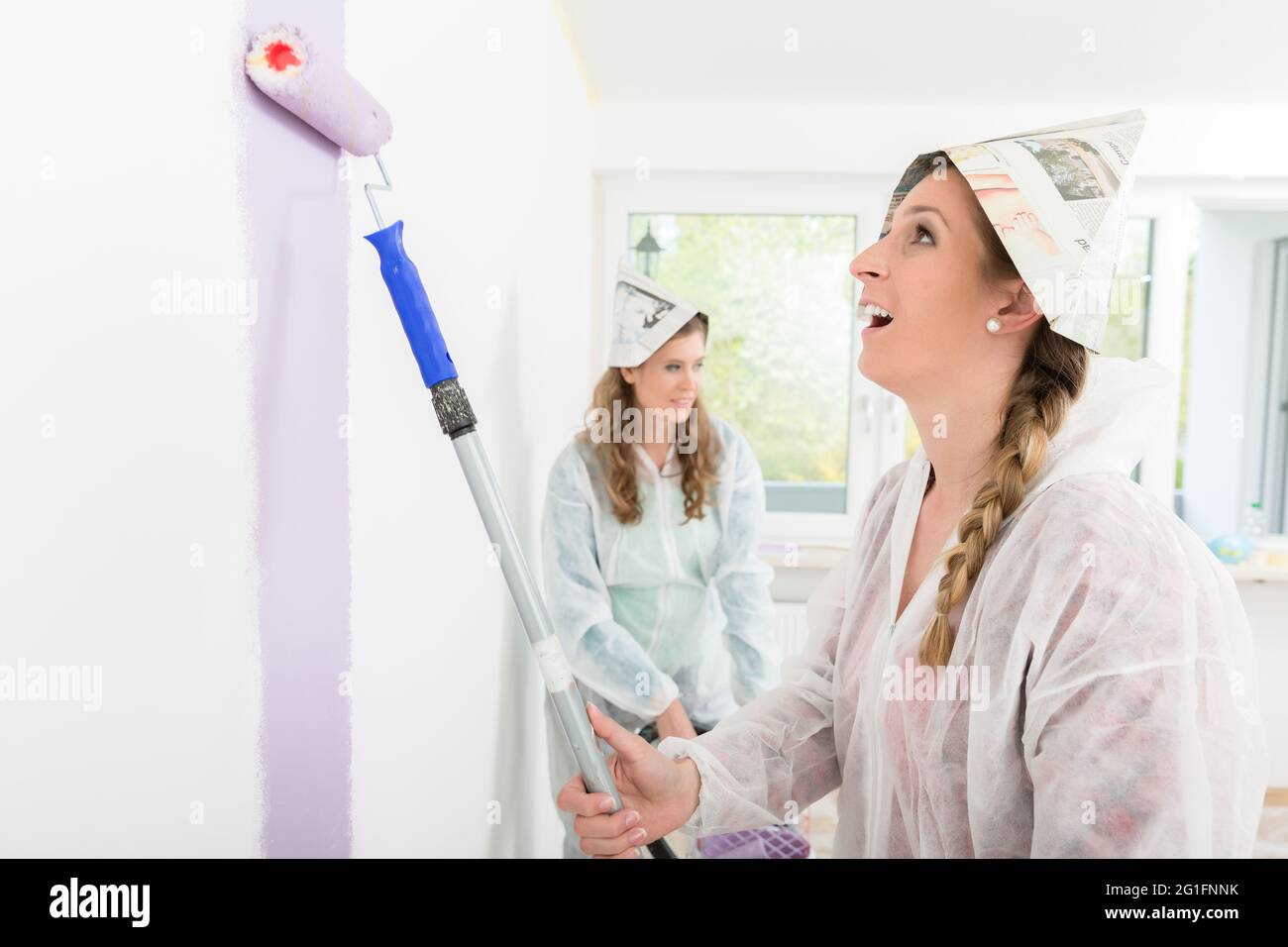 Eine Arbeiterin trägt einen Papierhut und malt die Wand mit einer Walze Stockfoto