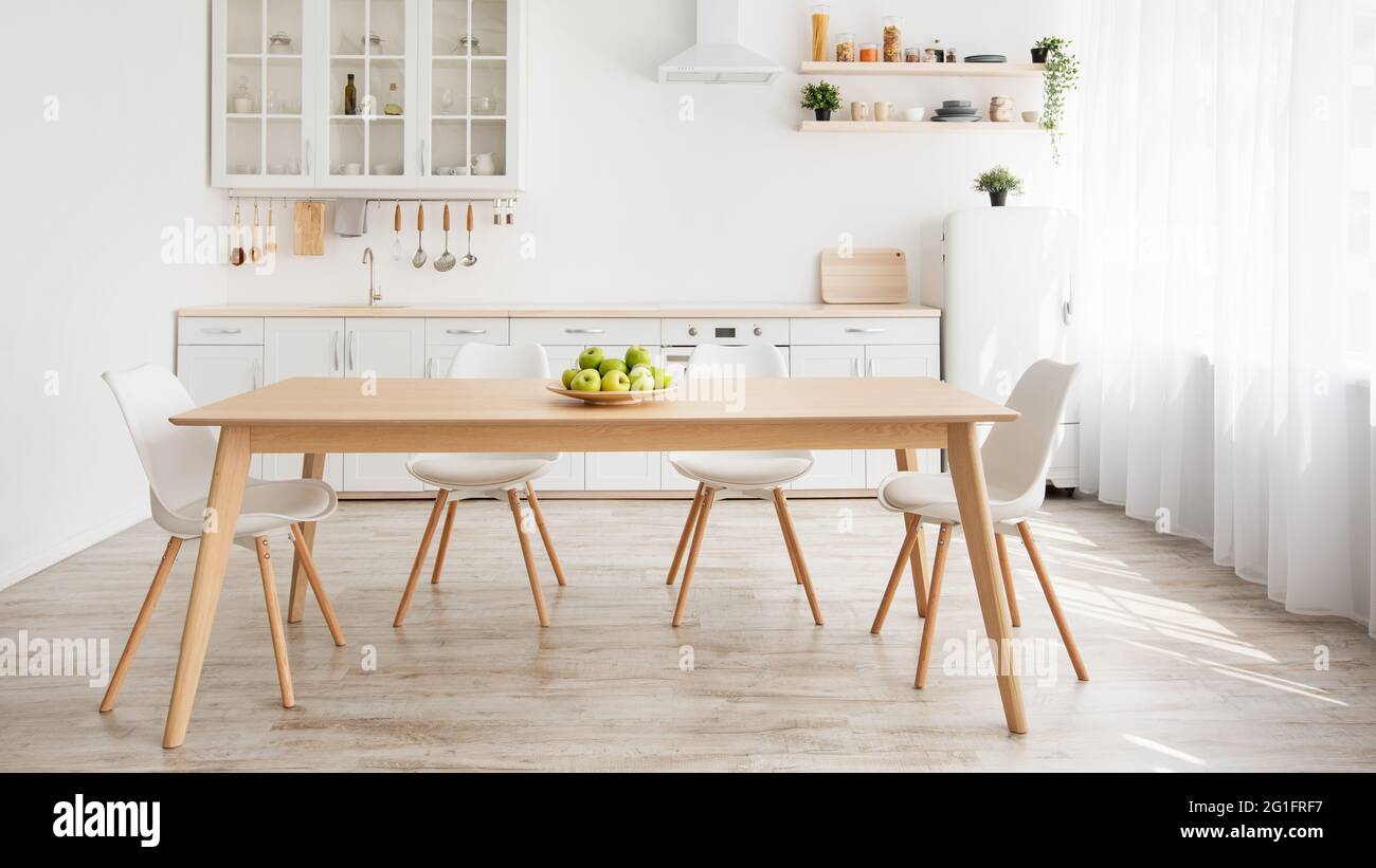 Skandinavische Innenausstattung. Weiße und hölzerne Küchenmöbel, Teller mit Äpfeln auf dem Esstisch, Panorama Stockfoto