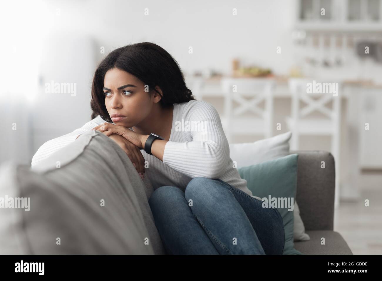 Einsame depressive afroamerikanische Frau, die mit traurigem Gesichtsausdruck auf der Couch sitzt und wegschaut, freien Raum Stockfoto