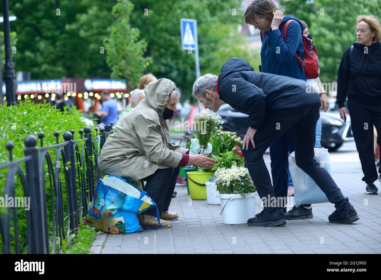 Mann Käufer riecht Blumen von einer alten Frau Blumenverkäufer auf der Straße der Stadt Stockfoto