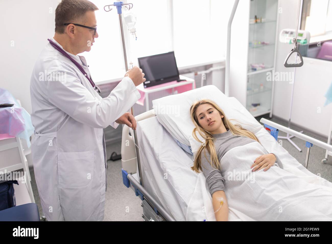 Der Arzt schließt die Dropper an. Der Patient liegt im Bett des Krankenhauses, während er behandelt wird. Stockfoto