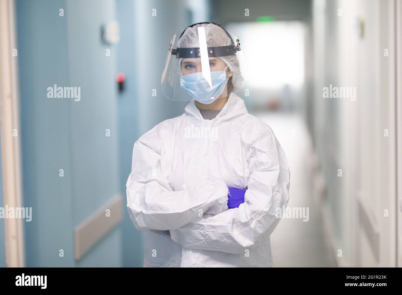 Während einer Coronavirus-Pandemie passt die junge Krankenschwester ihren Gesichtsschutz am Krankenhauskorridor an. Porträt des professionellen Mediziners am Arbeitsplatz. Er Stockfoto