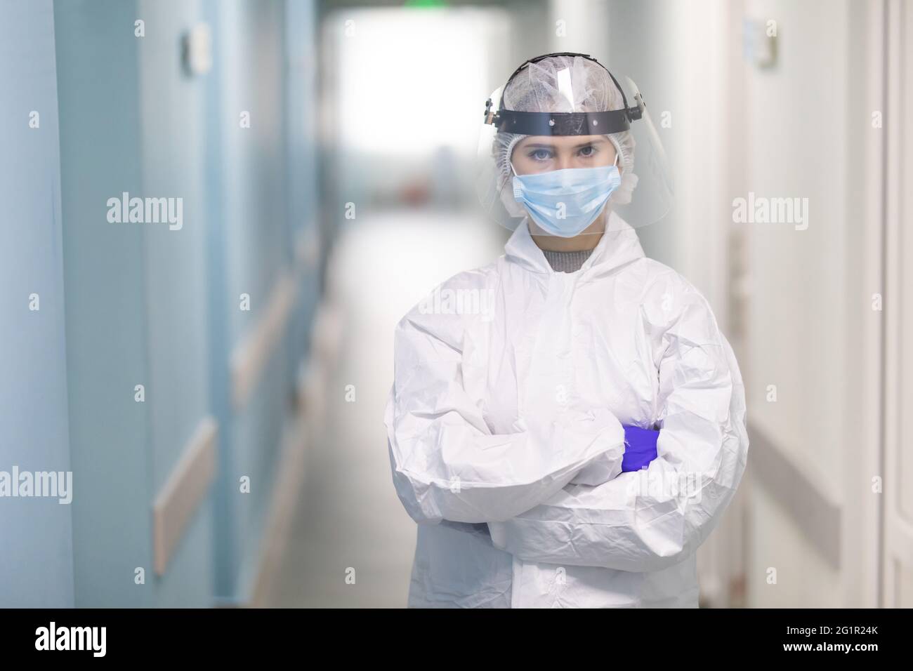 Während einer Coronavirus-Pandemie passt die junge Krankenschwester ihren Gesichtsschutz am Krankenhauskorridor an. Porträt des professionellen Mediziners am Arbeitsplatz. Er Stockfoto