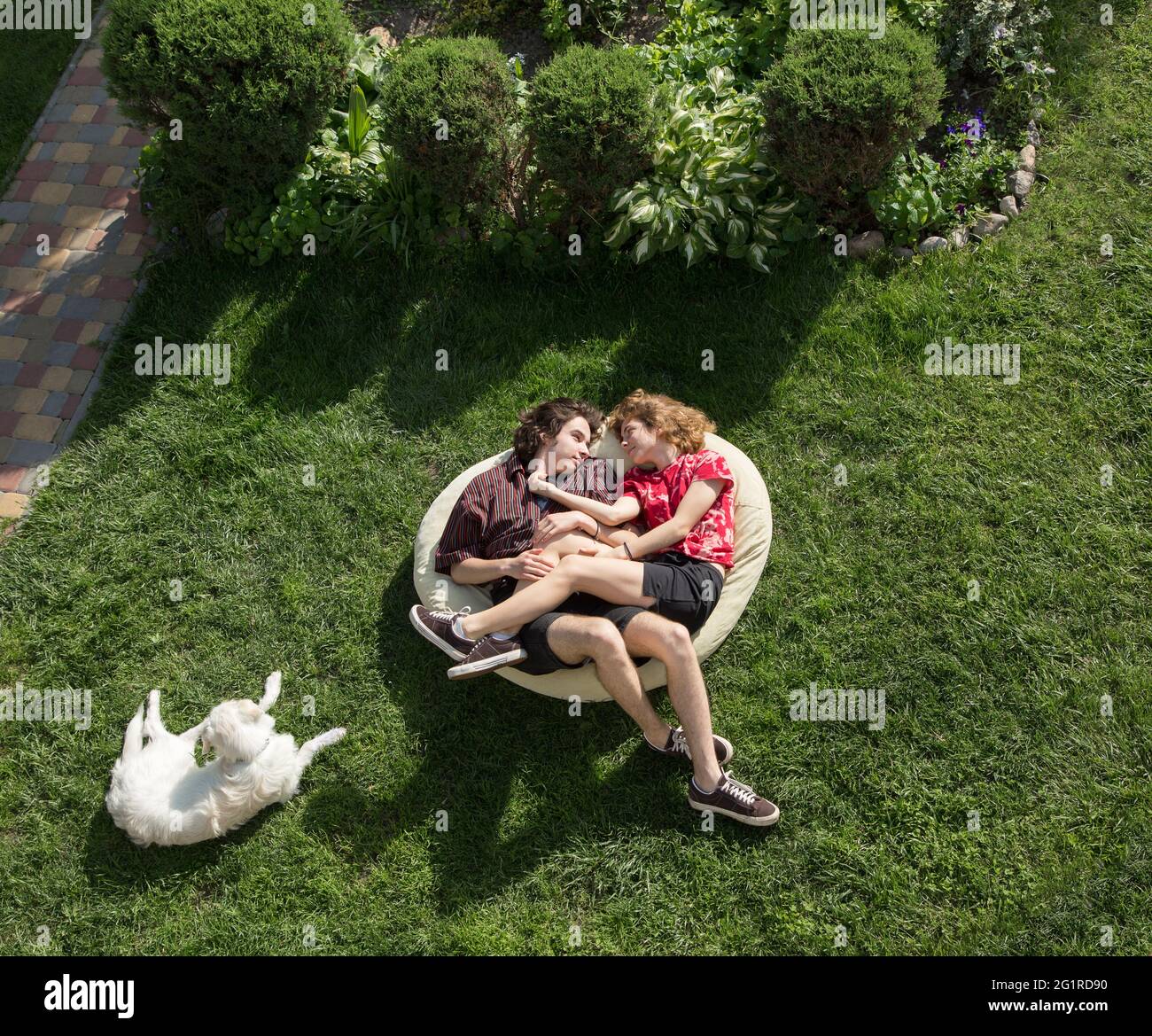 Jugendliche im Alter von 16-17 Jahren, ein Mann und ein Mädchen, liegen umarmt in einem großen weichen Beutel auf dem grünen Gras. Verliebte junge Menschen. Romantische Beziehung. Entspannen, Stockfoto