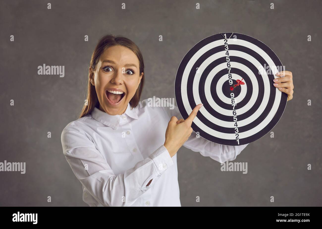 Porträt einer aufgeregten Geschäftsfrau, die mit dem Finger auf das Ziel zeigt, mit einem Pfeil direkt im Bullseye Stockfoto