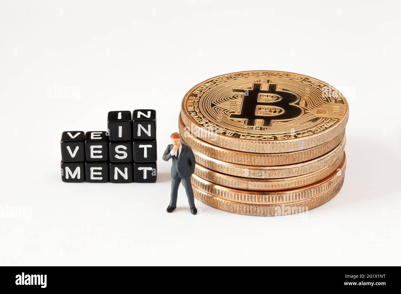 Würfel mit INVESTITIONSTEXT auf weißem Hintergrund. Geschäftsmann Figur denken in der Nähe von Würfeln mit Investition Wort, während in der Nähe Bitcoin Stapel stehen. Stockfoto