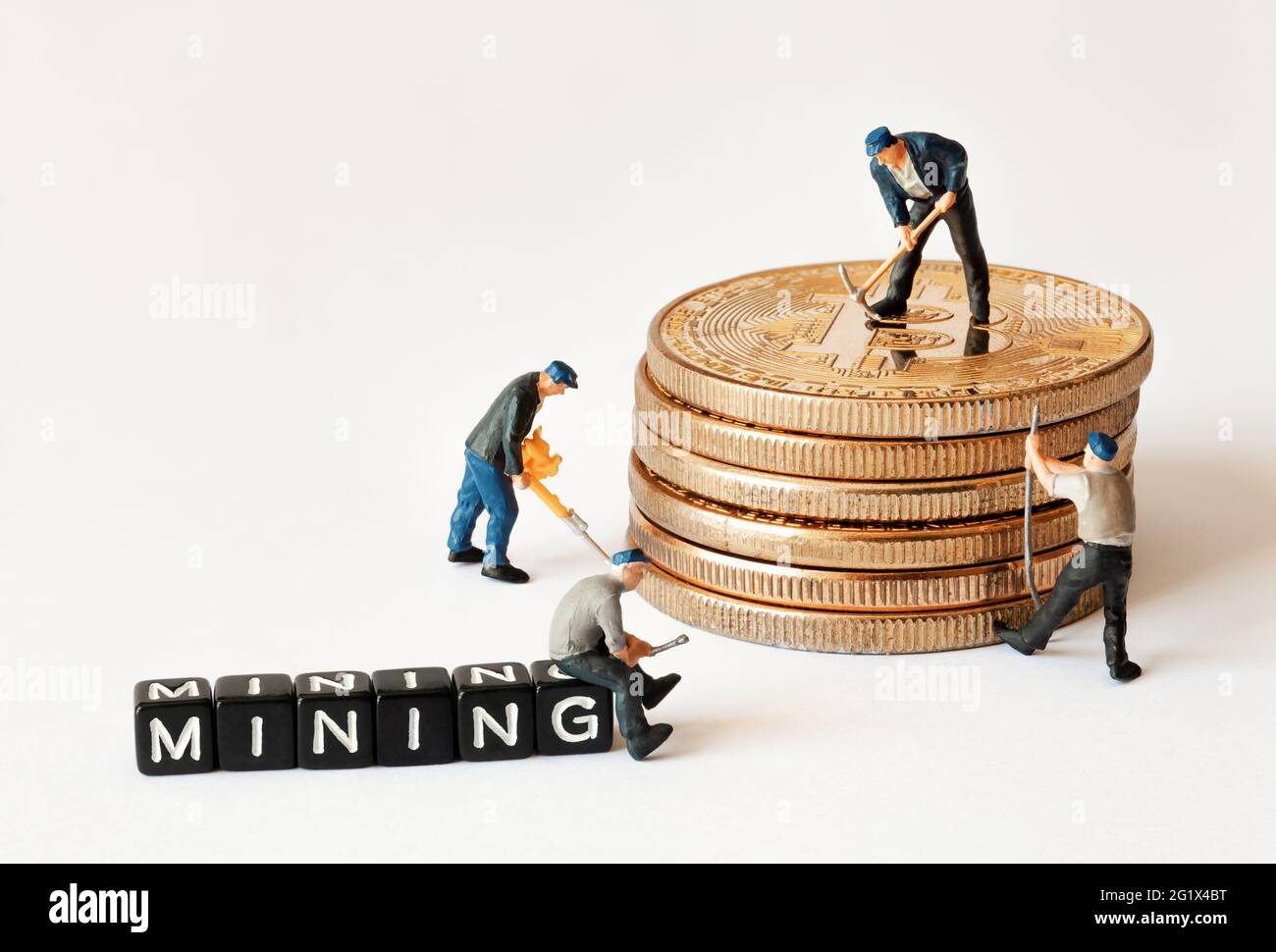 Gruppe von Bergarbeiterfiguren mit Ausrüstung, die an einem Stapel von Bitcoins in der Nähe von schwarzen Würfeln mit MINING-Text arbeitet. Stockfoto